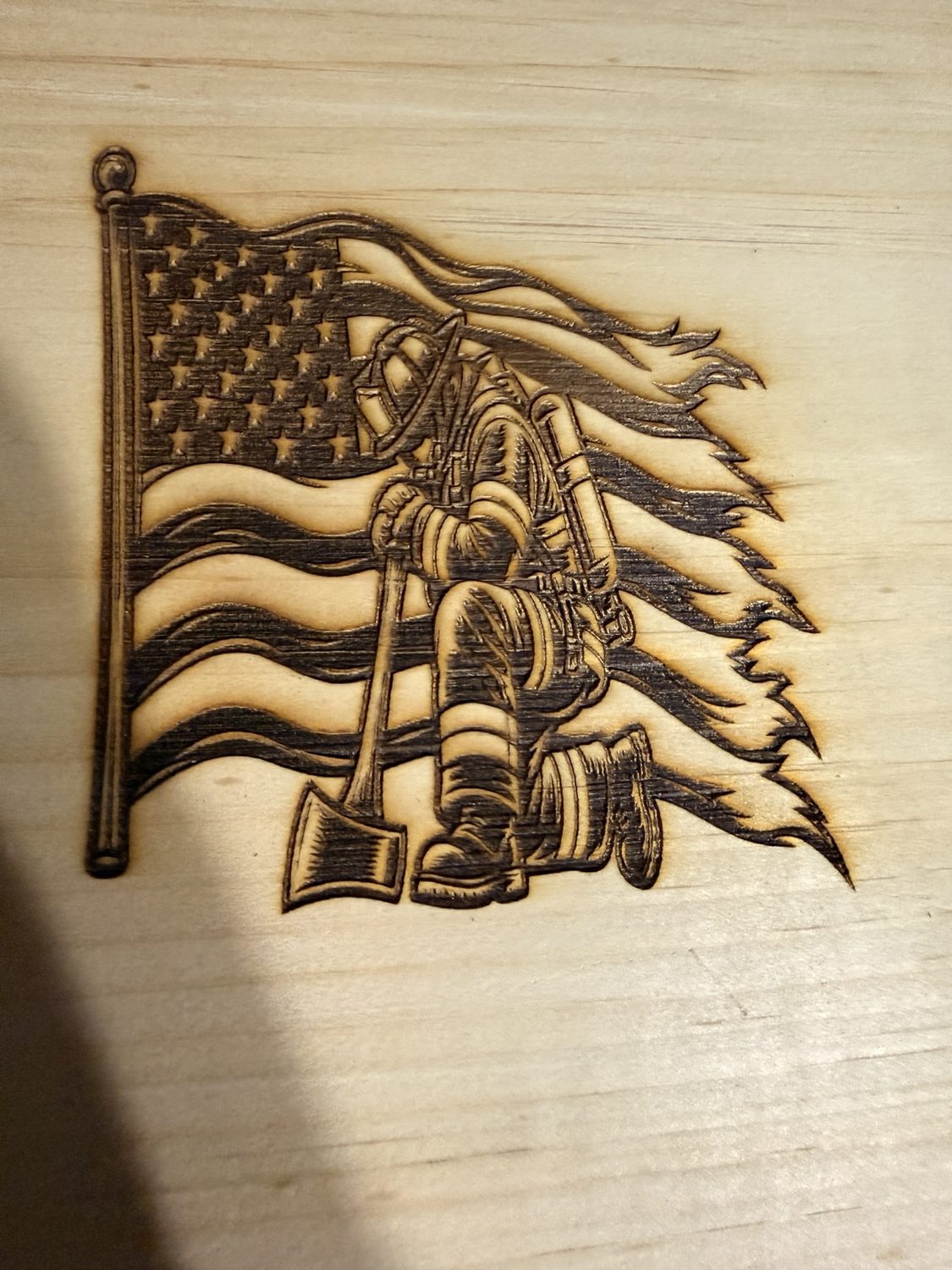 Wood engraving of a firefighter kneeling beside an American flag