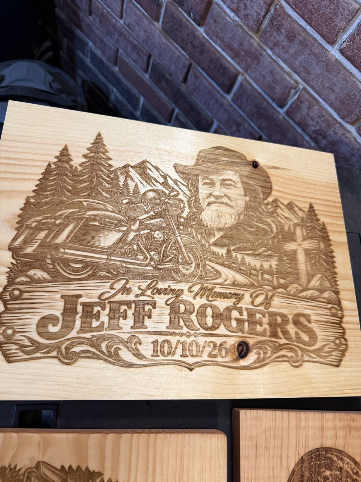 Wooden memorial plaque honoring Jeff Rogers, featuring his portrait, motorcycle, and mountain scenery
